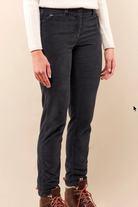 A person wearing slim-fit dark charcoal gray jeans, a white ribbed knit sweater, and brown lace-up boots, standing against a plain beige studio background.