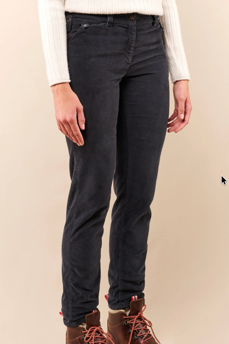 A person wearing slim-fit dark charcoal gray jeans, a white ribbed knit sweater, and brown lace-up boots, standing against a plain beige studio background.