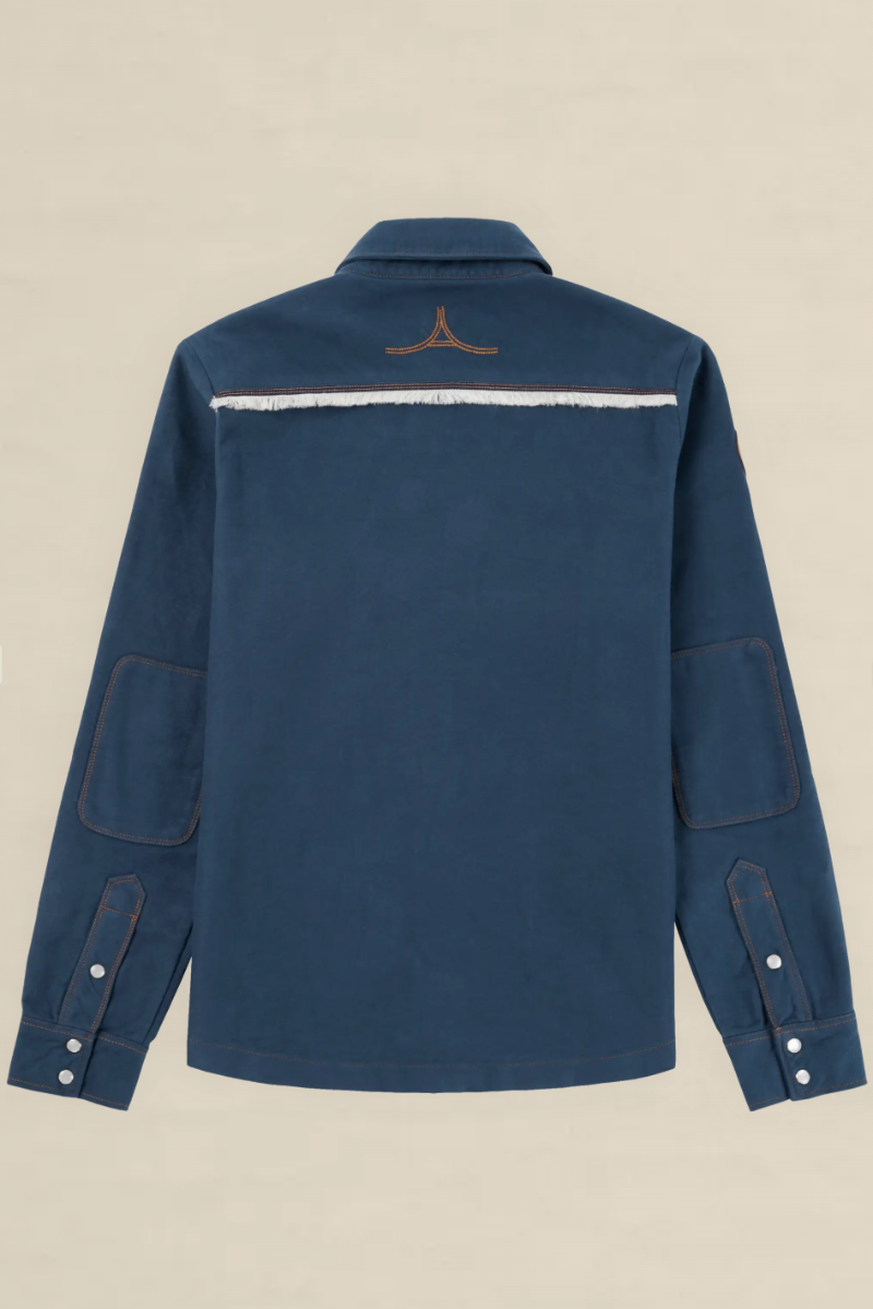 A navy blue long-sleeve shirt jacket shown from the back, featuring a horizontal white stripe across the upper back with a small brown embroidered logo above it, set against a solid beige background.
