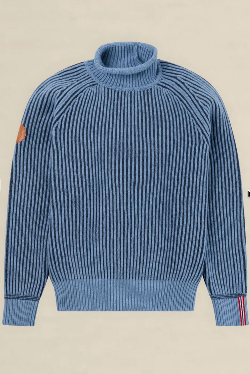 A blue ribbed knit turtleneck sweater with a brown leather patch on the left sleeve and thin red and white stripes on the right sleeve cuff, shown flat against a light beige background.