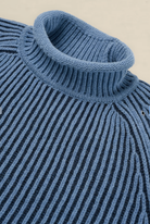 Close-up of a ribbed knit turtleneck sweater in a dusty medium blue color, showing the detailed knit texture and collar.
