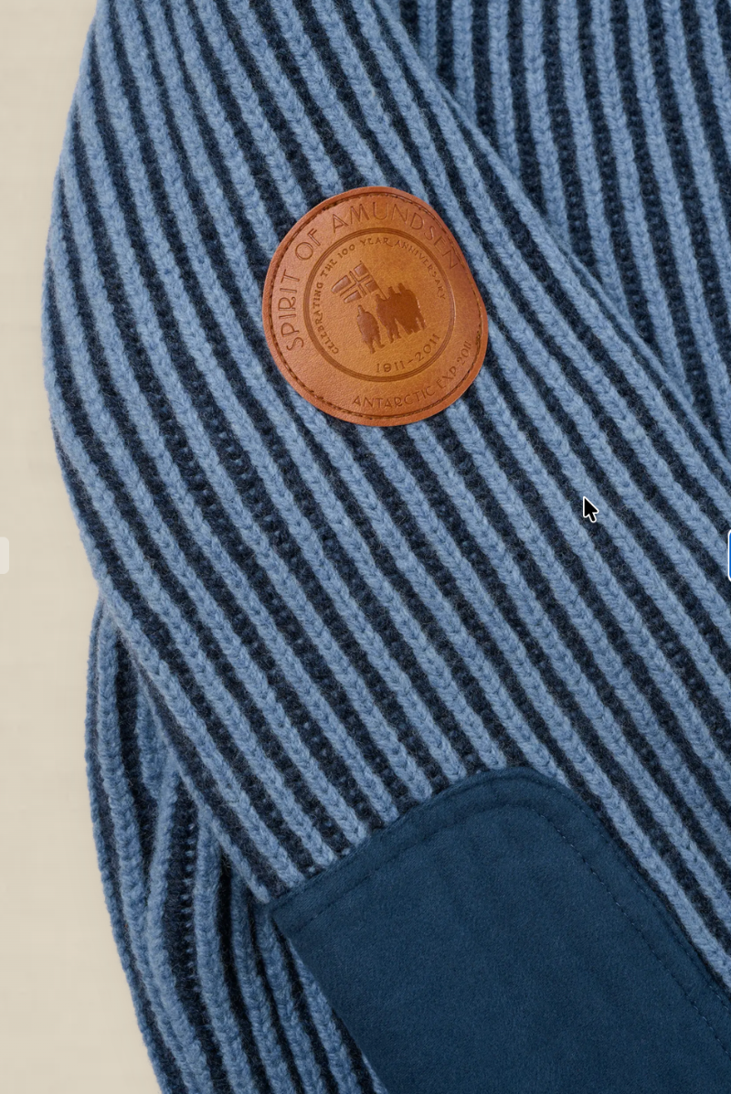 Close-up of a blue and navy striped knit garment with a round brown leather patch reading 'SUPPORT OF ALL VOLS' and a dark navy patch pocket.