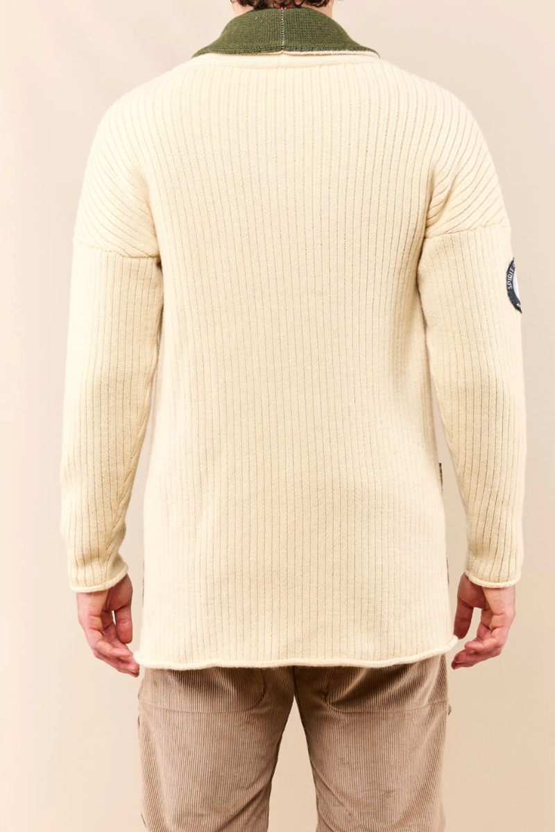 A person shown from the back wearing a cream ribbed knit sweater with an olive green collar, paired with tan pants, against a plain beige studio background.