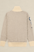 A cream-colored knit sweater with a dense black geometric pattern, featuring a ribbed mock neck, cuffs, and hem, with a circular patch on the right sleeve, shown against a solid light beige background.