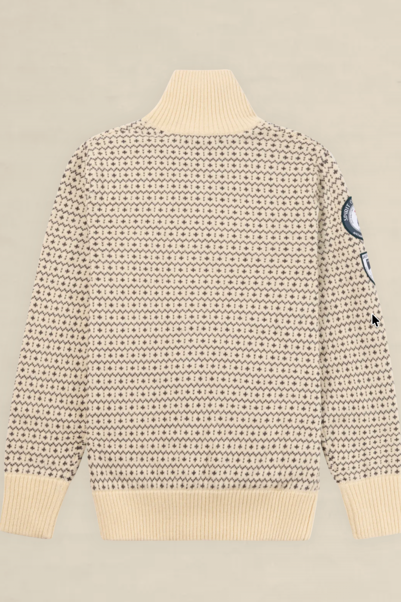 A cream-colored knit sweater with a dense black geometric pattern, featuring a ribbed mock neck, cuffs, and hem, with a circular patch on the right sleeve, shown against a solid light beige background.
