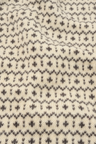 Close-up of a cream-colored knit fabric with a dark gray Fair Isle pattern of small geometric motifs.