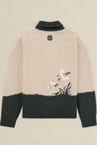 Back view of a knit sweater in beige and dark green, featuring a small embroidered floral motif near the lower right side and a circular black logo patch at the neck.