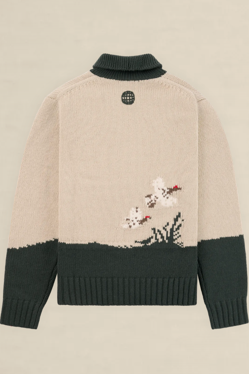 Back view of a knit sweater in beige and dark green, featuring a small embroidered floral motif near the lower right side and a circular black logo patch at the neck.