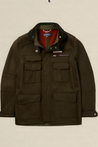 A dark olive green waxed cotton jacket with a corduroy collar, multiple front flap pockets, and a red inner lining, shown against a solid light beige background.