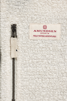 Close-up of a textured off-white fleece jacket featuring a black metal zipper with a matching beige fabric pull tab and a sewn-on brand label reading 'AMUNDSEN SPORTS FIELD TESTING ADVENTURES'.