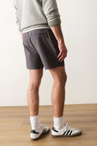 Person wearing gray shorts and white socks with black Adidas shoes on a wooden floor.