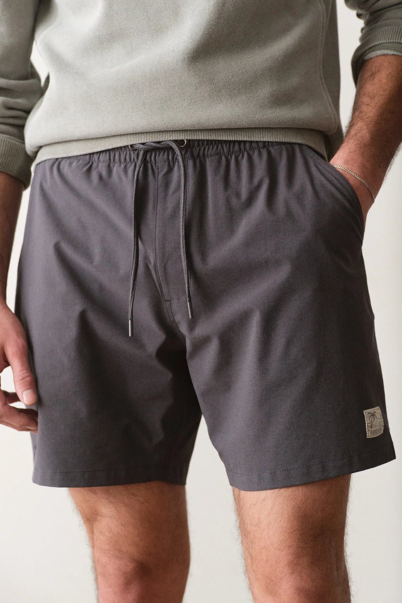 Person wearing gray shorts with a small logo on a plain background