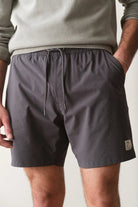 Person wearing gray shorts with a small logo on a plain background