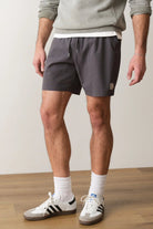 Person wearing gray athletic shorts and white sneakers on a plain background