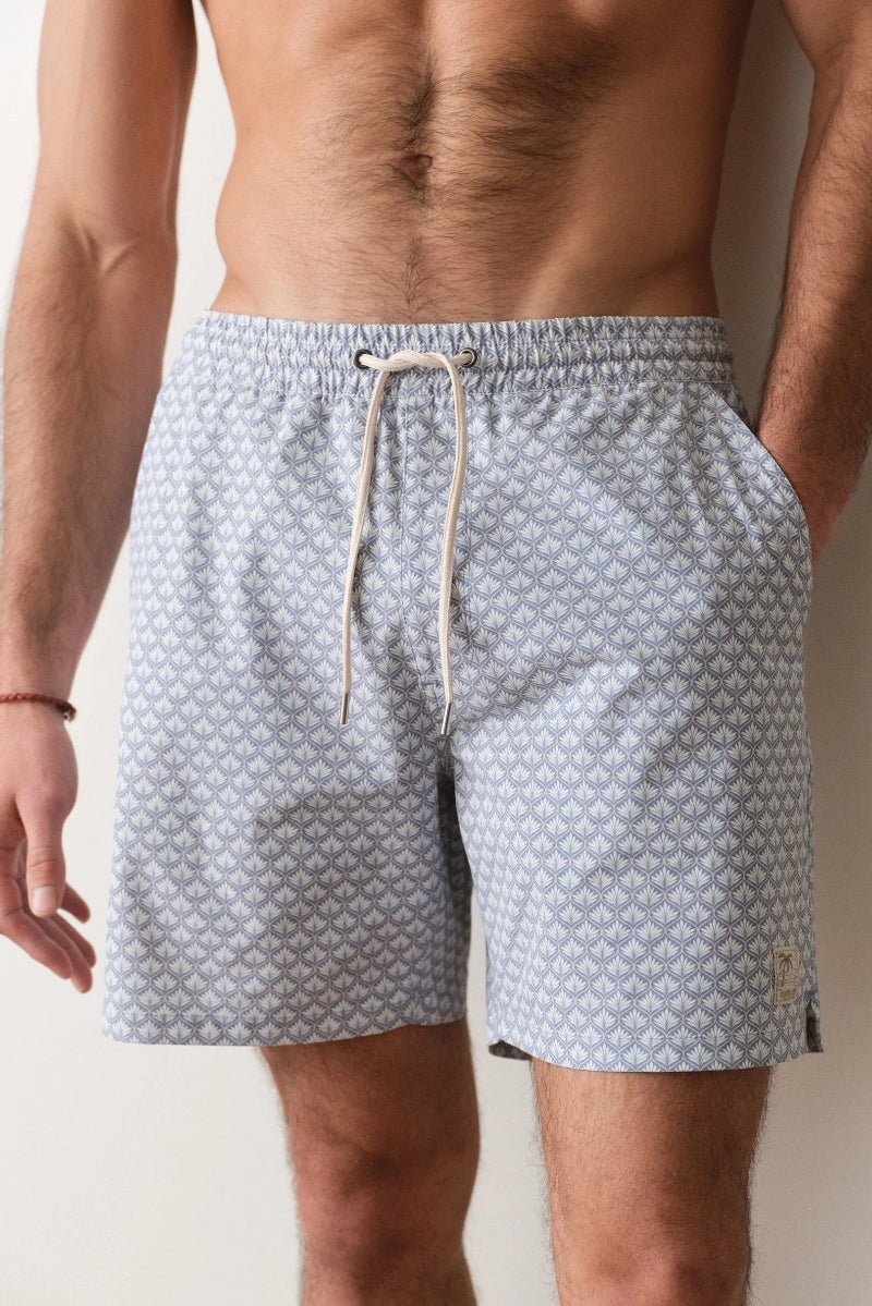 Man wearing patterned swim shorts against a neutral background