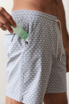 Person wearing patterned shorts with a product in the pocket against a neutral background