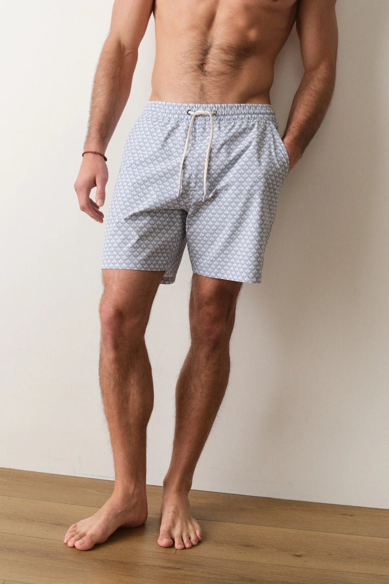 Man wearing patterned shorts standing against a plain wall.