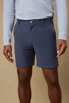 Person wearing navy shorts and a light gray long-sleeve shirt against a beige background