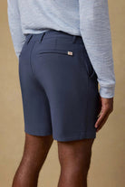 Person wearing navy shorts and a light gray long-sleeve shirt against a beige background