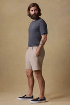 Man wearing a gray t-shirt and beige shorts against a beige background
