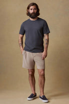 Man wearing a dark gray t-shirt and beige shorts against a brown background