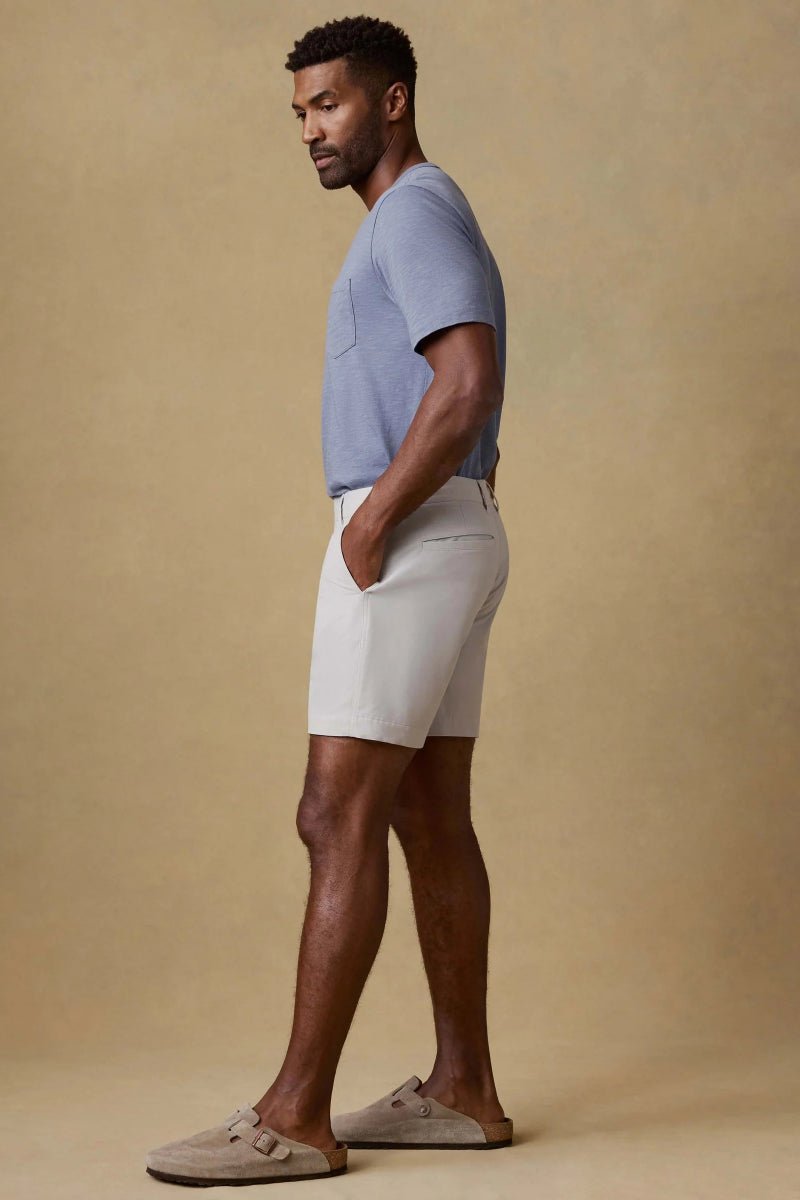 Man wearing a light blue shirt and beige shorts against a beige background