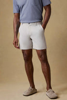 Person wearing light-colored shorts and a blue shirt against a beige background