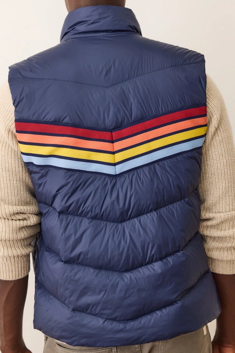 Blue puffer vest with colorful stripes worn by a person on a plain background