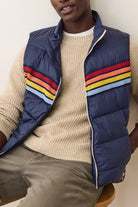 Person wearing a blue puffer vest with colorful stripes over a beige sweater.