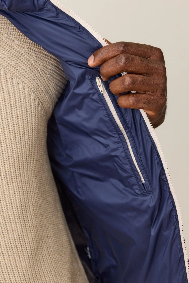 Hand zipping a navy blue jacket over a beige garment on a neutral background