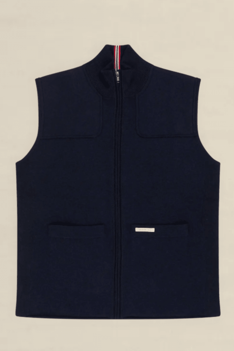 A navy blue zip-up fleece vest with a mock neck, two front patch pockets, and a small white brand label on the lower front pocket, shown flat against a light beige background.