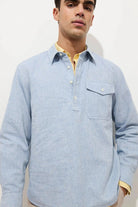 Man wearing a light blue long-sleeve shirt with a yellow collar against a white background