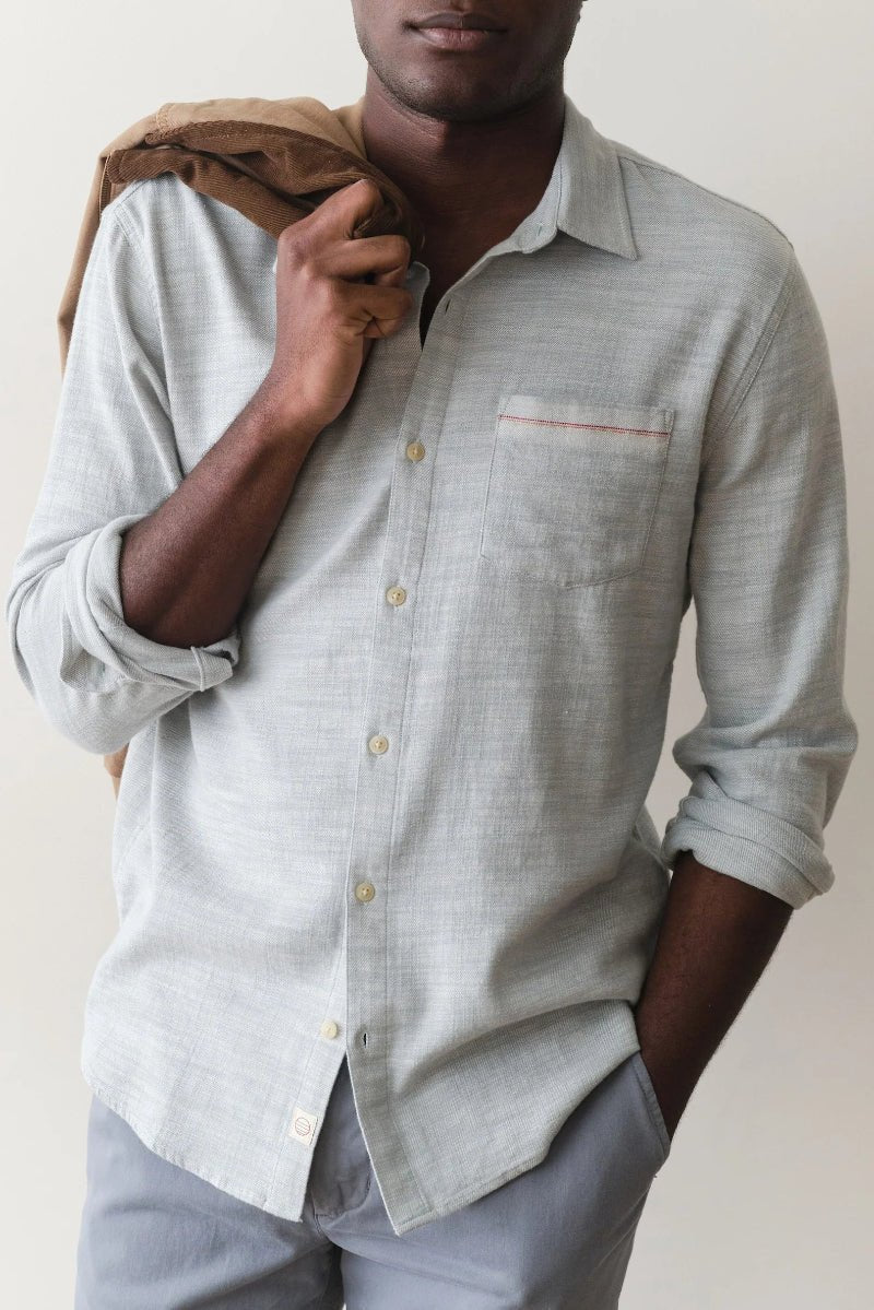 Man wearing a light gray button-up shirt with rolled-up sleeves against a plain background