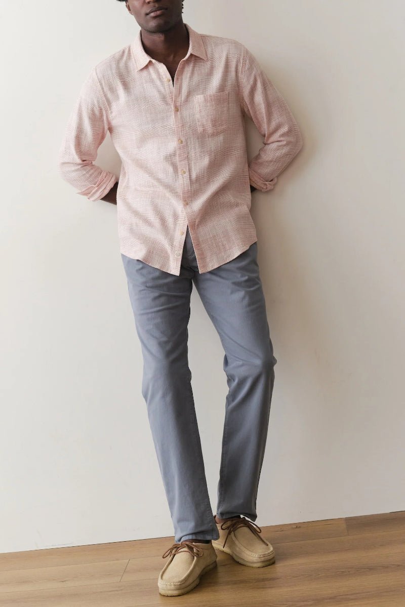Person wearing a pink shirt and gray pants against a white wall.