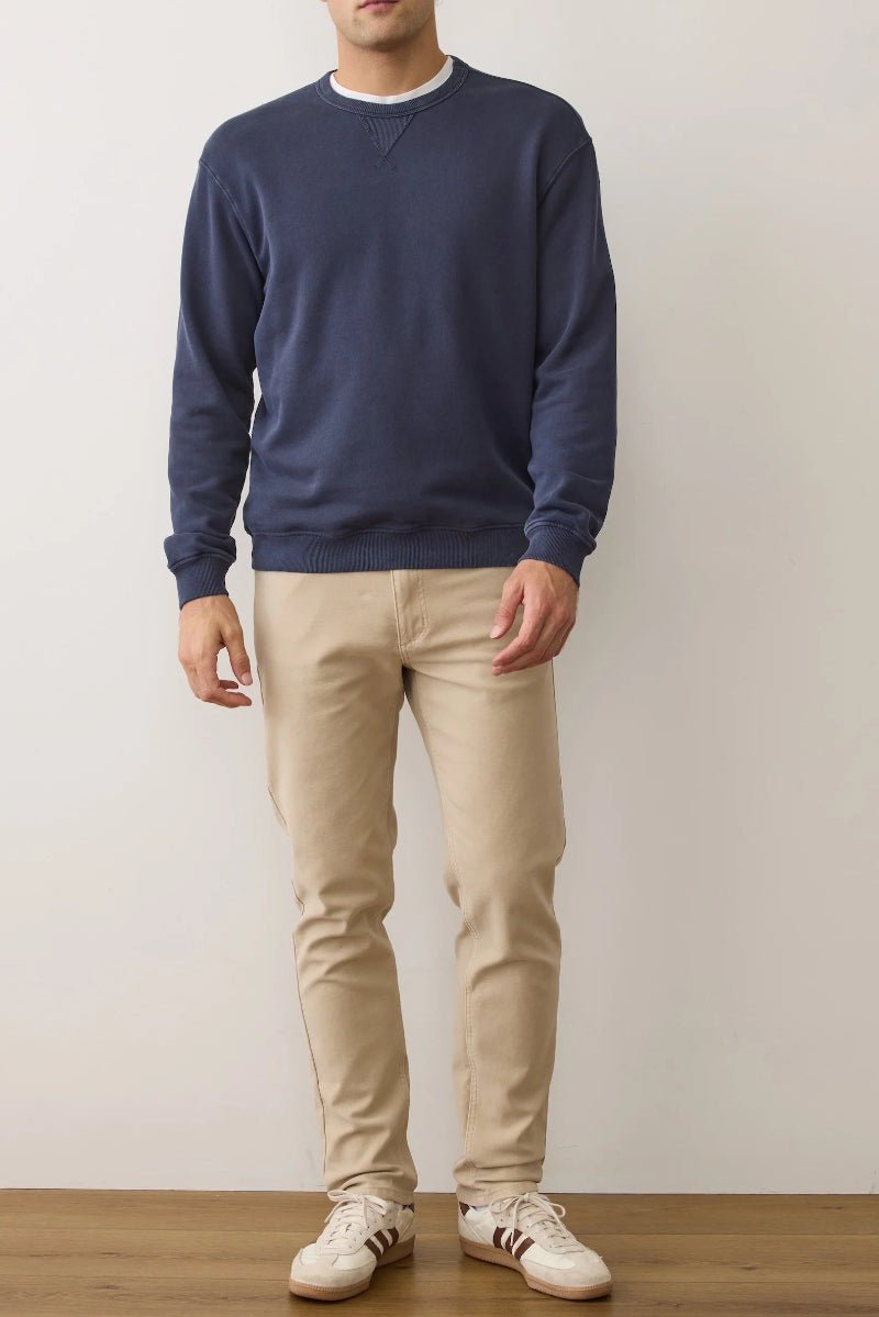 Person wearing a navy sweater and beige pants standing against a plain background