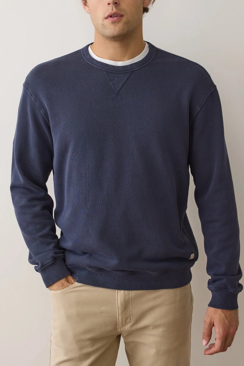 Man wearing a navy blue sweatshirt and beige pants against a plain background