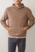 Person wearing a brown hoodie and dark pants against a plain background