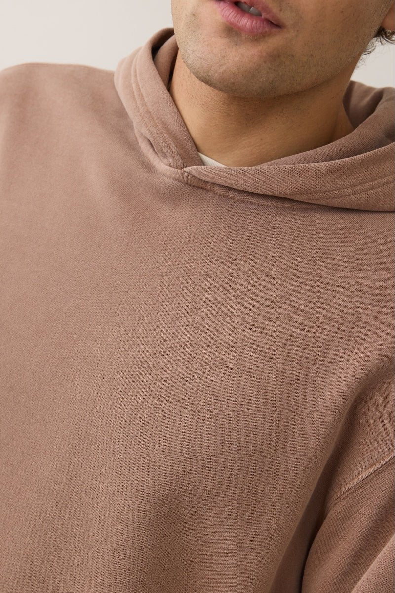 Close-up of a person wearing a brown hoodie against a neutral background