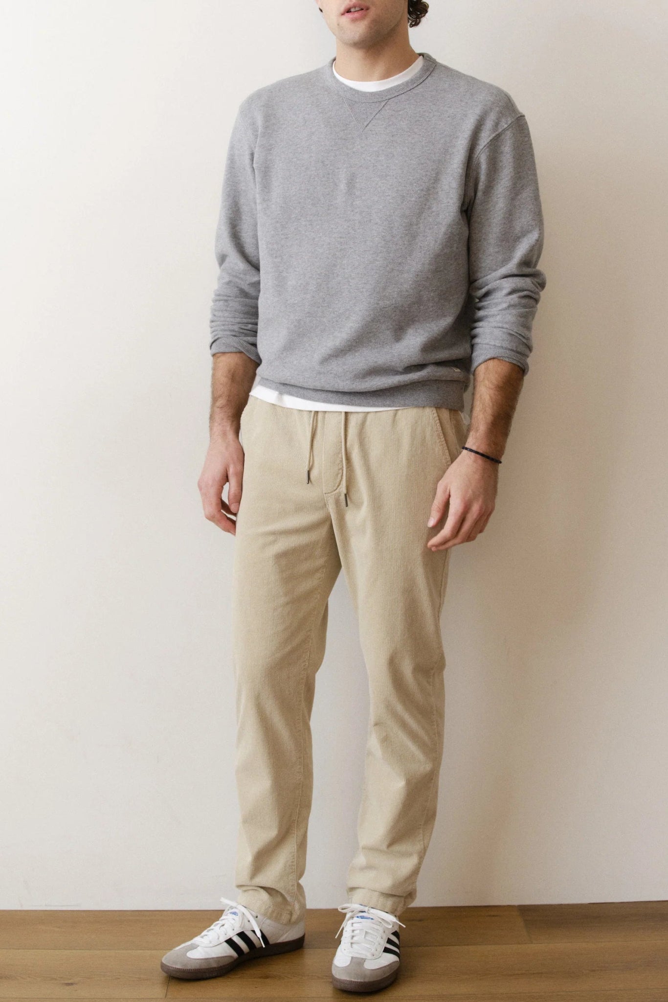 Person wearing a gray sweater, beige pants, and Adidas shoes against a plain background
