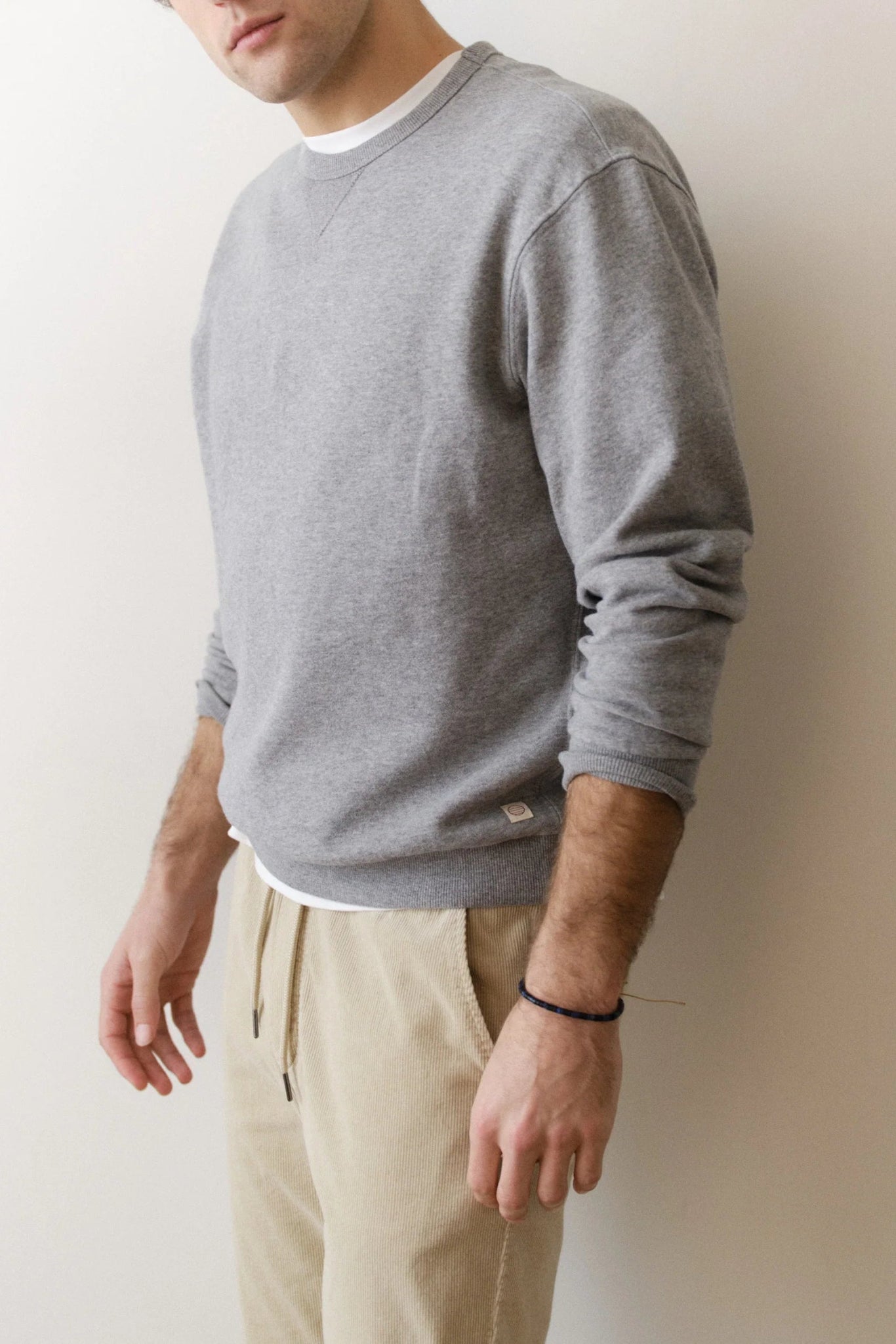 Person wearing a gray sweatshirt and beige pants against a plain background