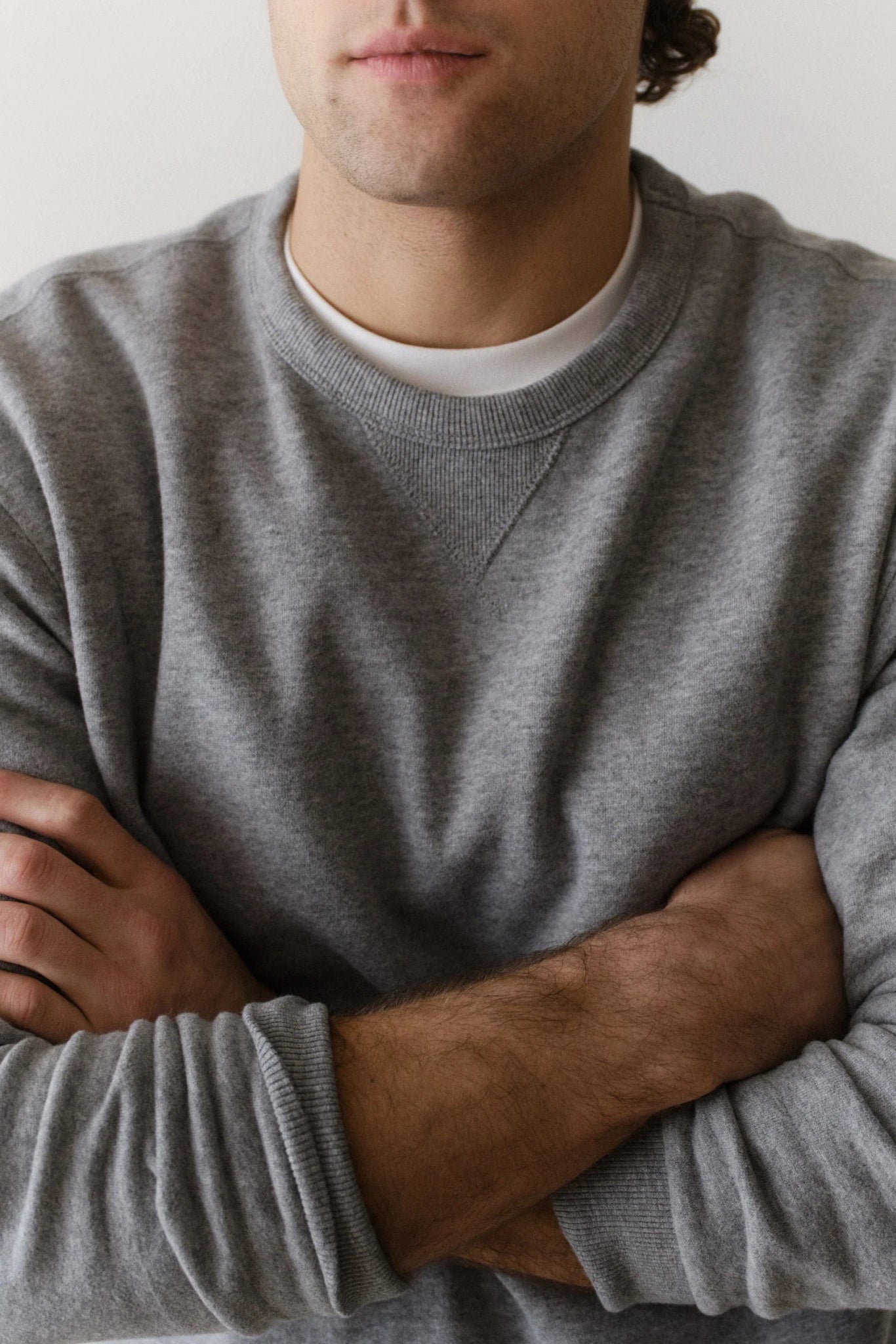 Man wearing a gray sweater with arms crossed against a neutral background