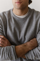 Man wearing a gray sweater with arms crossed against a neutral background