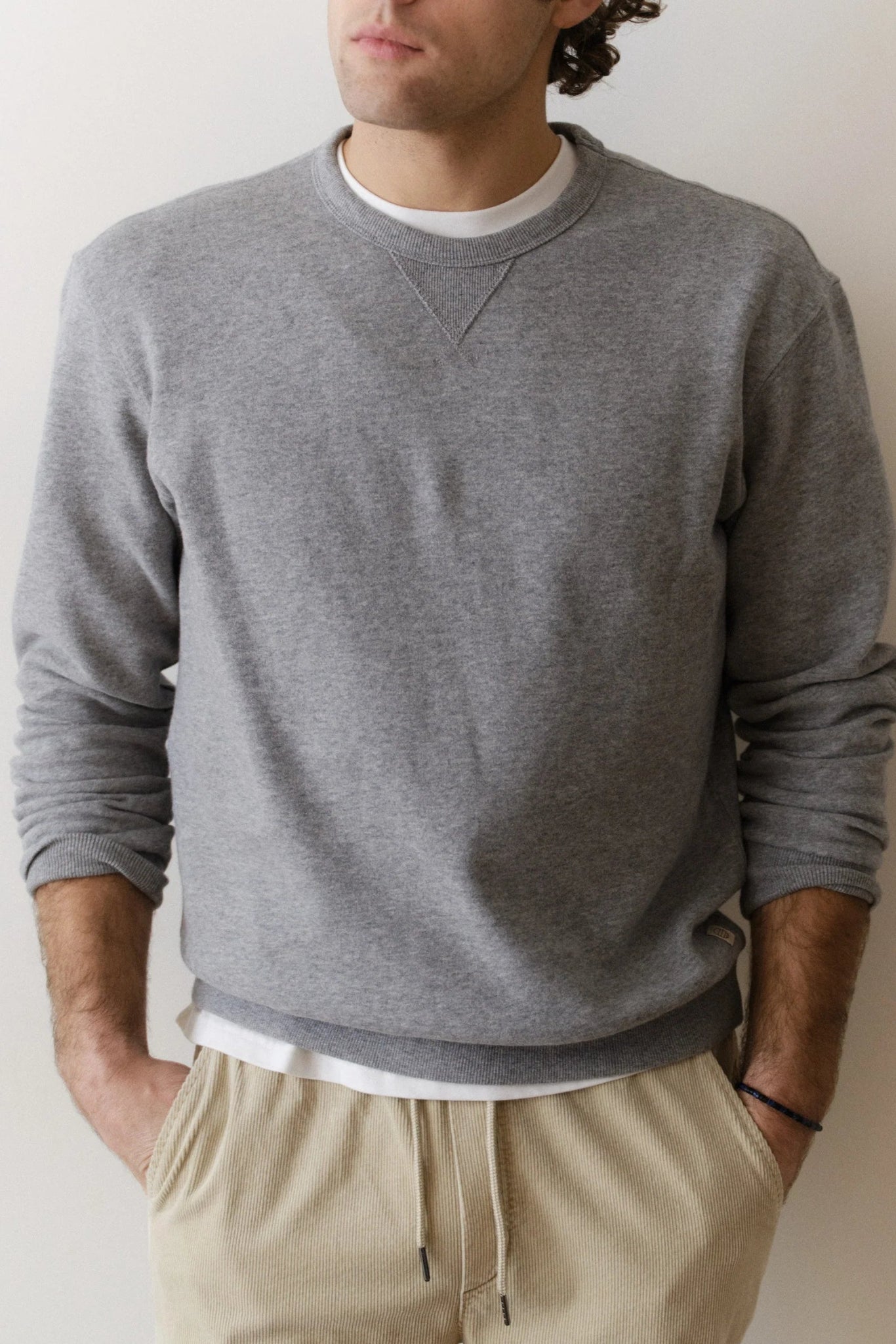 Person wearing a gray sweatshirt and beige pants against a plain background