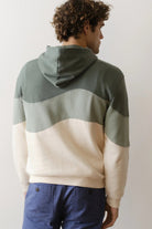 Person wearing a color-blocked hoodie with green and beige sections on a plain background