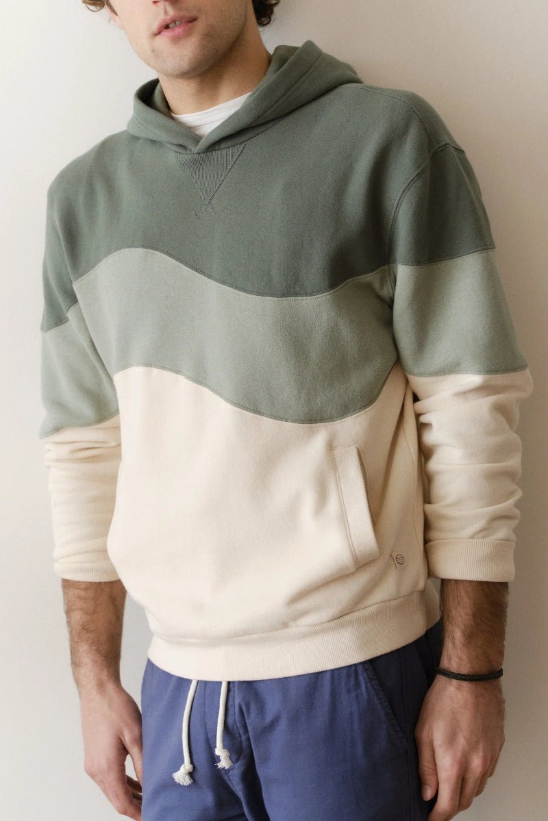 Person wearing a green and beige color-blocked hoodie with blue pants against a plain background