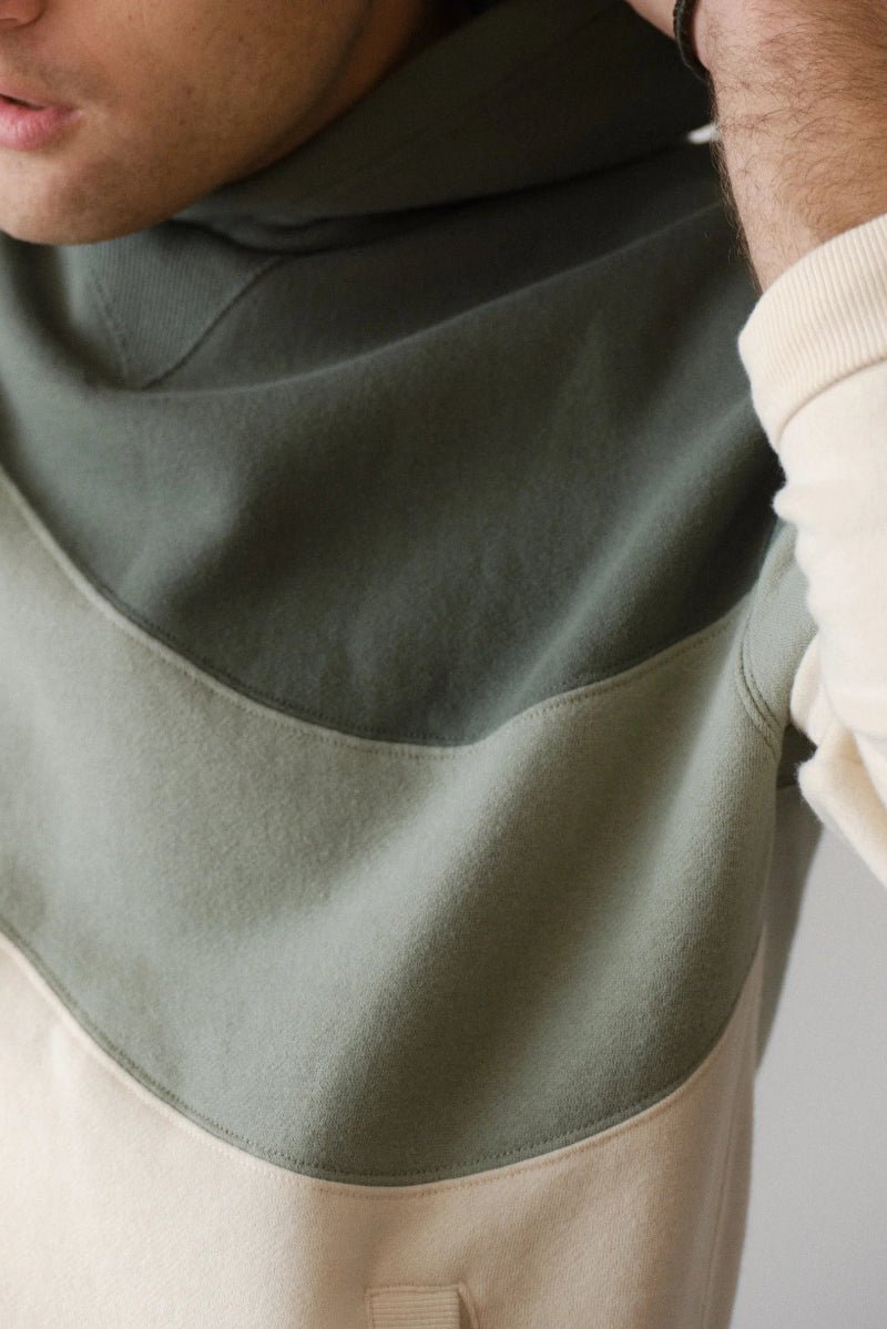 Person wearing a green and beige color-blocked hoodie with a neutral background