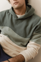 Person wearing a green and beige color-blocked hoodie against a neutral background