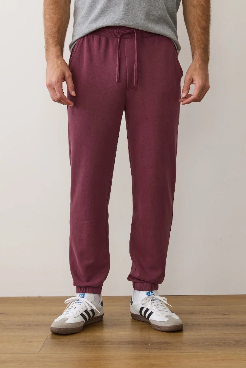 Person wearing maroon sweatpants and white sneakers on a plain background