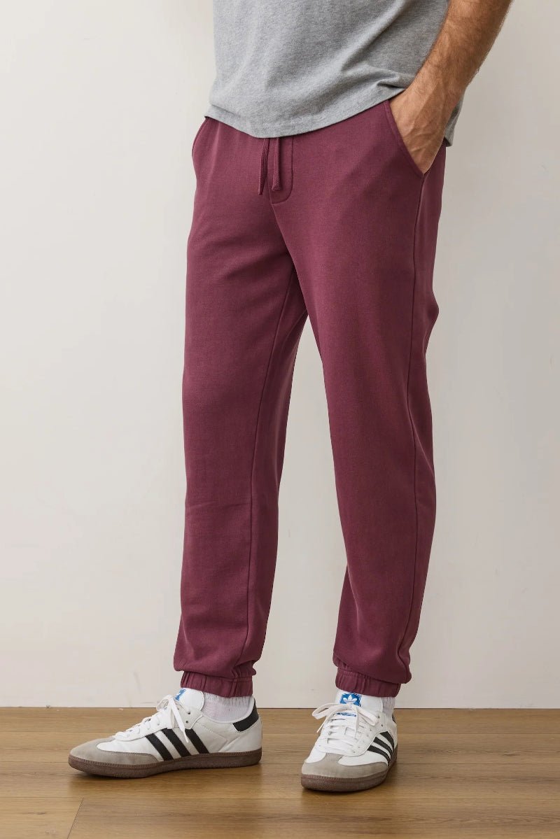 Person wearing maroon jogger pants and white sneakers with black stripes on a plain background