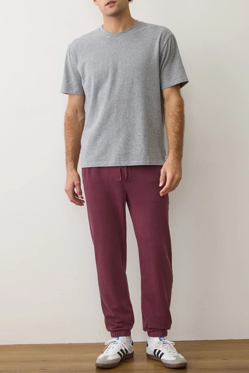 Person wearing a gray t-shirt and maroon pants with white sneakers on a plain background